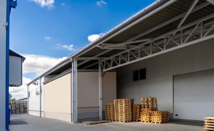 Galpão comercial com área externa organizada e pallets empilhados, ilustrando opções de salas e galpões para alugar para diferentes tipos de negócio.